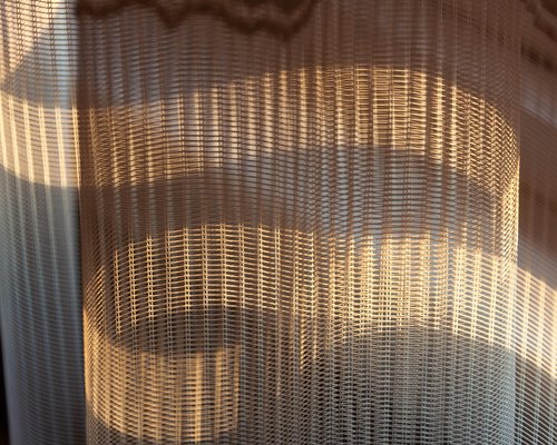 A desk positioned perpendicular to a window with soft sheer curtains diffusing bright sunlight